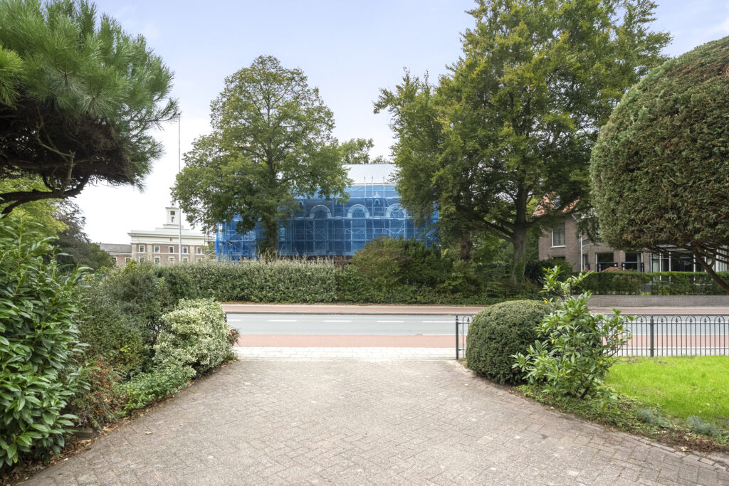 Building with blue scaffolding and surrounding greenery.
