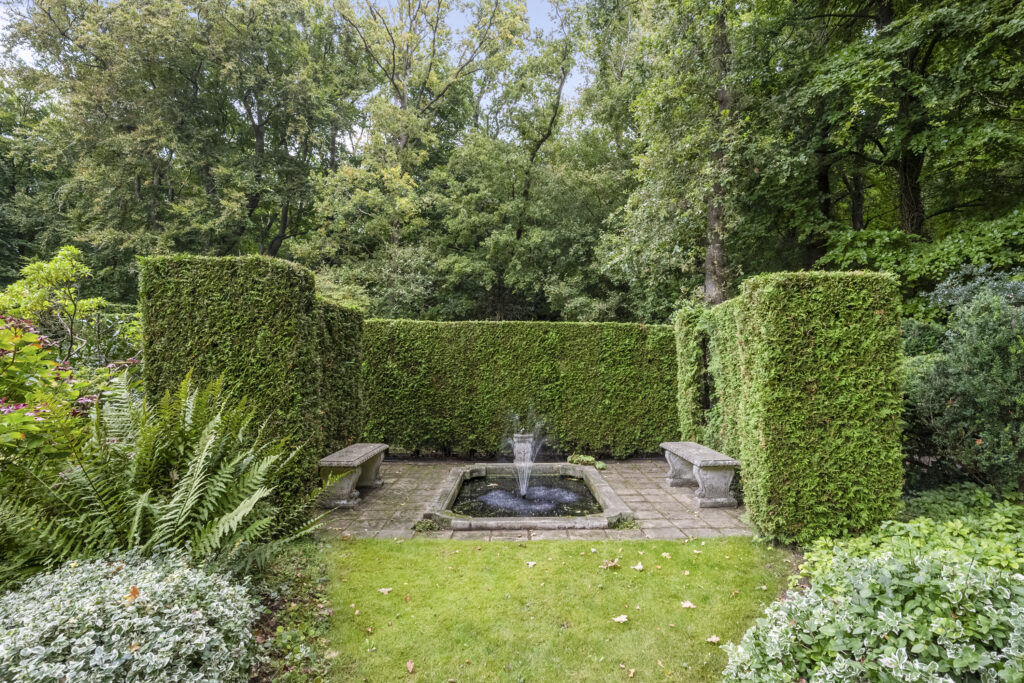 Garden with hedges, fountain, and benches.