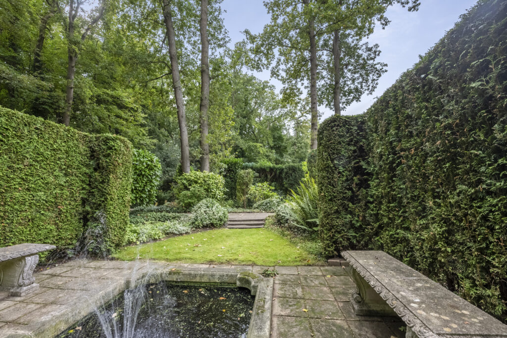 Tranquil garden with hedge, benches, and fountain.