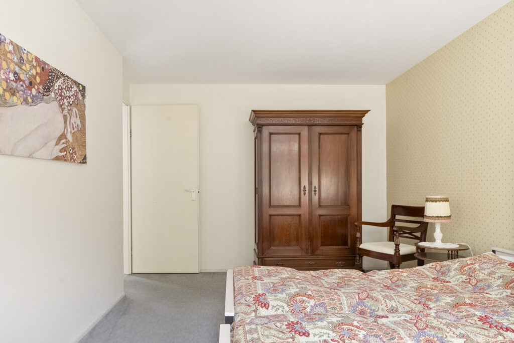Cozy bedroom with wooden wardrobe and patterned bedspread.