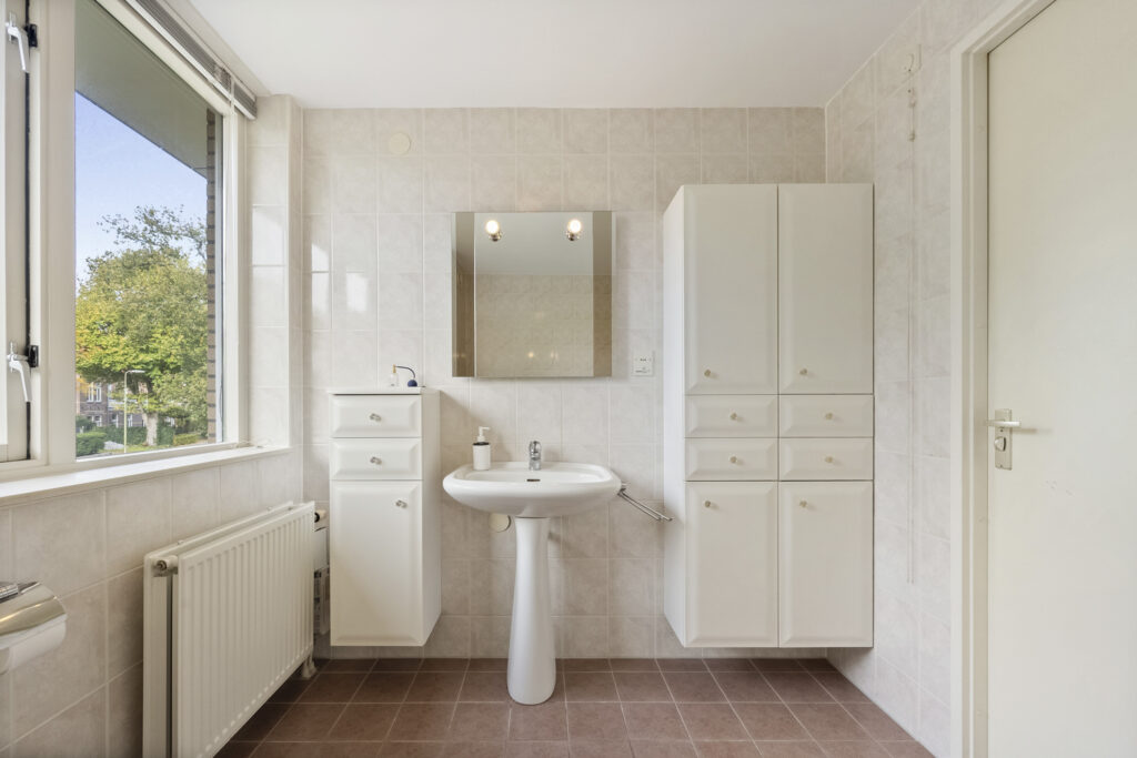 Bright bathroom with white cabinets and pedestal sink.
