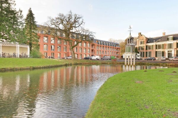 Historic brick building by serene pond with tower.