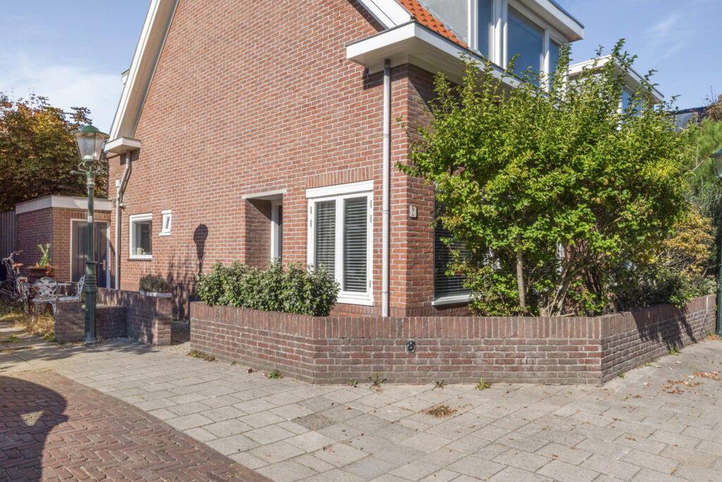 Red brick house with greenery and sidewalk.