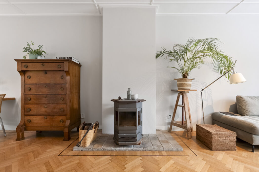Cozy living room with stove, plants, and wooden furniture.