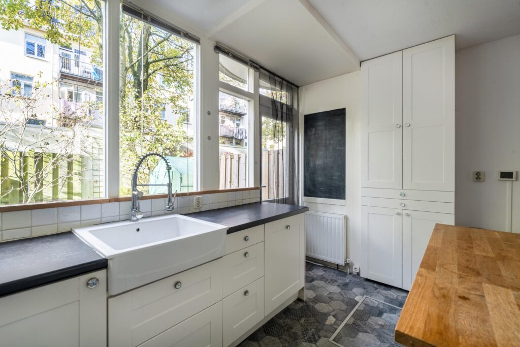 Bright kitchen with large windows and white cabinets.