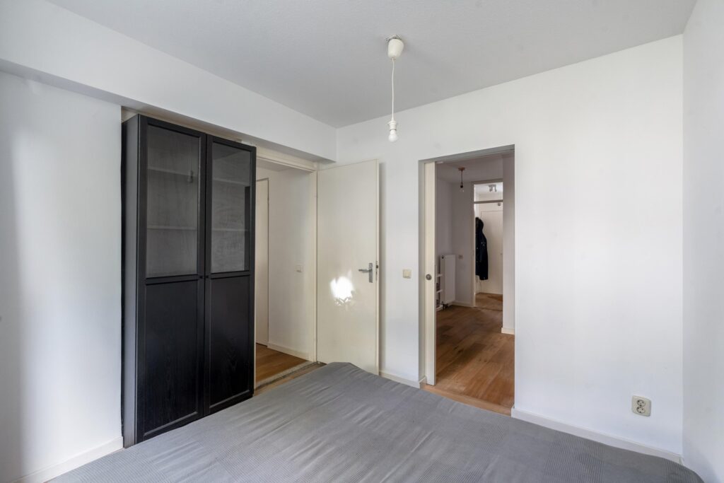Minimalist bedroom with black wardrobe and white walls.