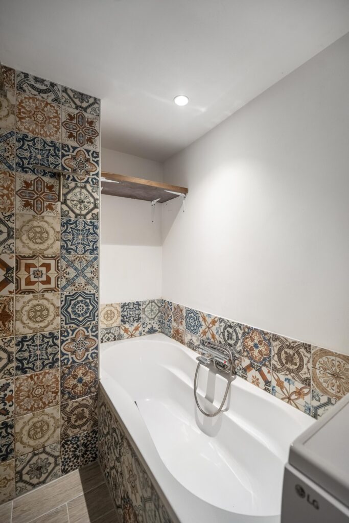 Bathroom with decorative patterned tiles and white bathtub.
