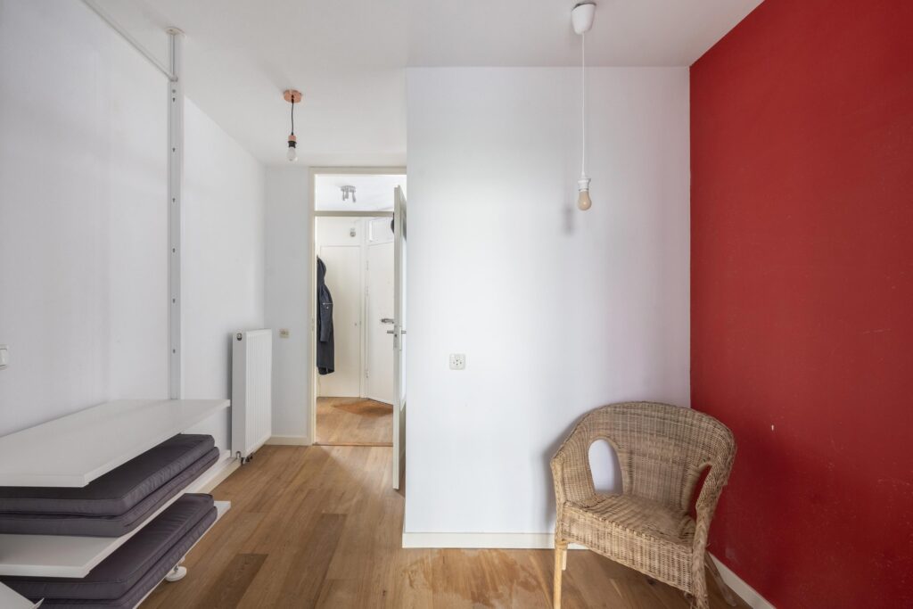 Minimalist hallway with red accent wall and wicker chair.