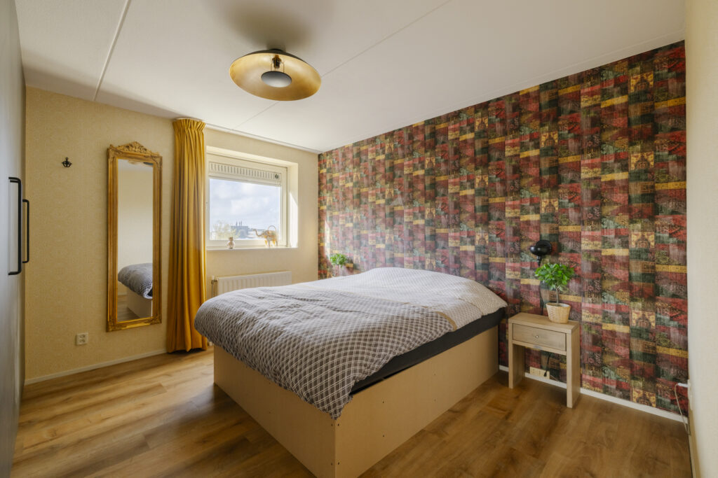 Cozy bedroom with patterned accent wall and wooden flooring.