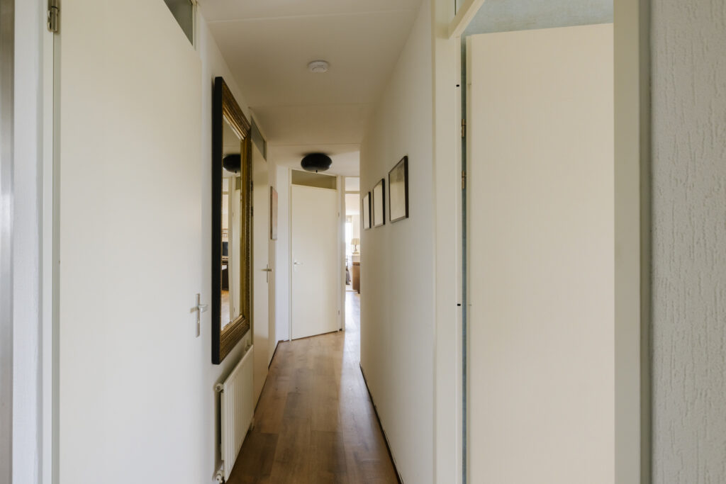 Narrow hallway with open door and framed mirror.
