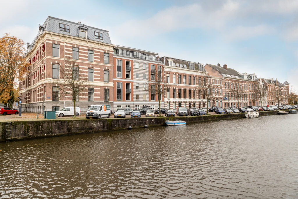 Historic buildings by a canal with cars parked.