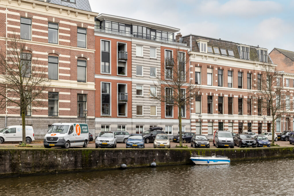 Colorful canal-side buildings with parked cars and van.
