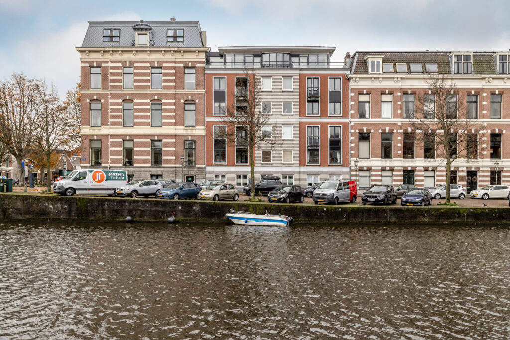 Historic riverside buildings with parked cars and canal.