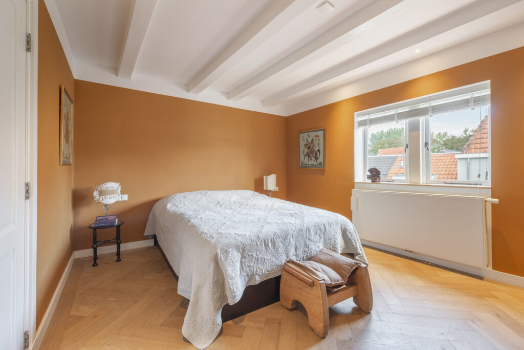 Cozy bedroom with orange walls and quilted bed.
