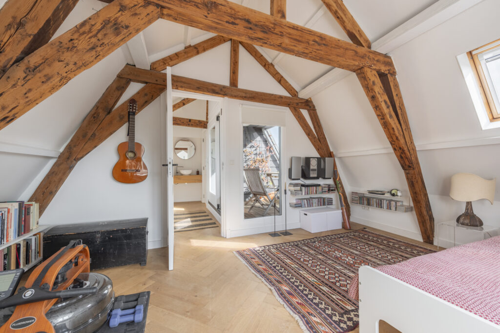 Cozy attic bedroom with wooden beams and guitar.