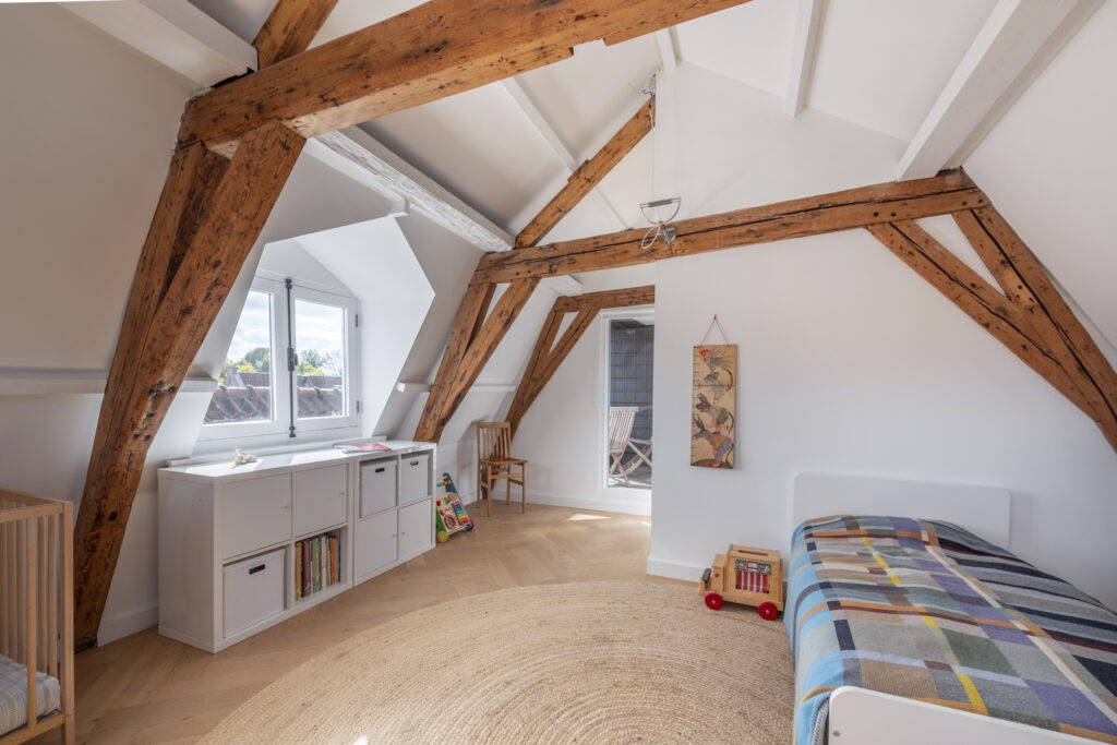 Attic room with wooden beams, bed, and shelves.