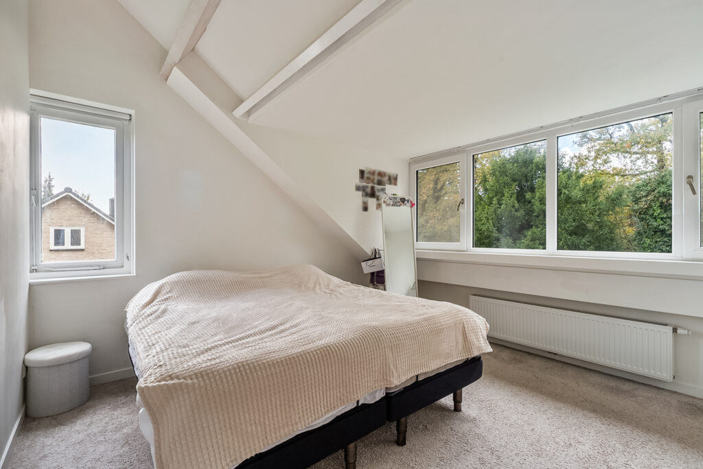 Cozy attic bedroom with big windows and beige bedding.
