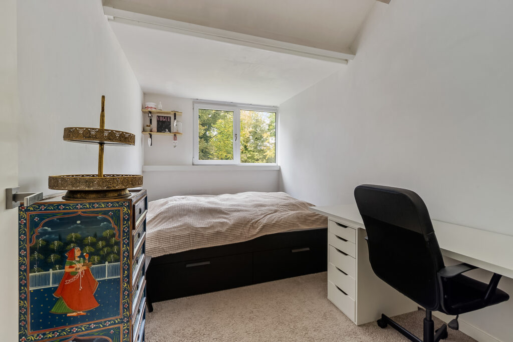 Cozy bedroom with bed, desk, and window view.