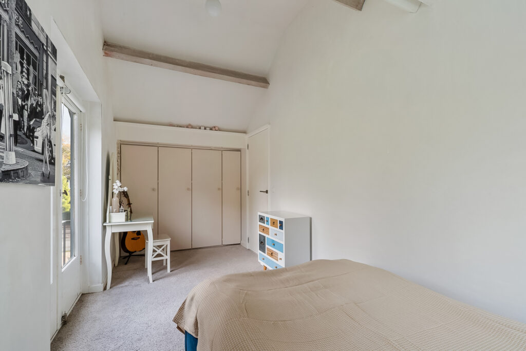 Simple bedroom with guitar, desk, and bed.