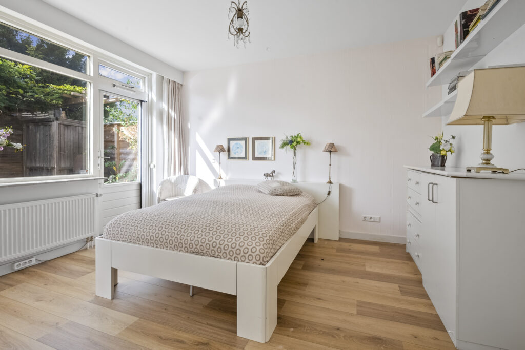 Bright bedroom with large window and wooden floor.