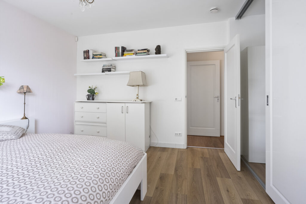 Minimalist bedroom with wooden floor and white furniture.