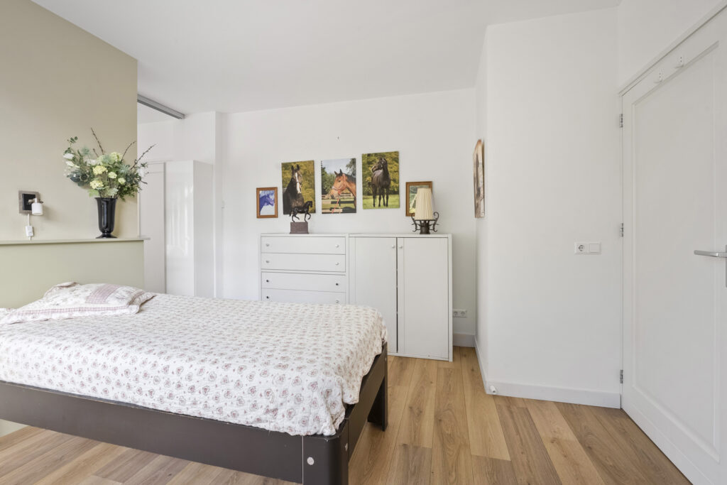 Cozy bedroom with bed, dresser, and paintings on wall.