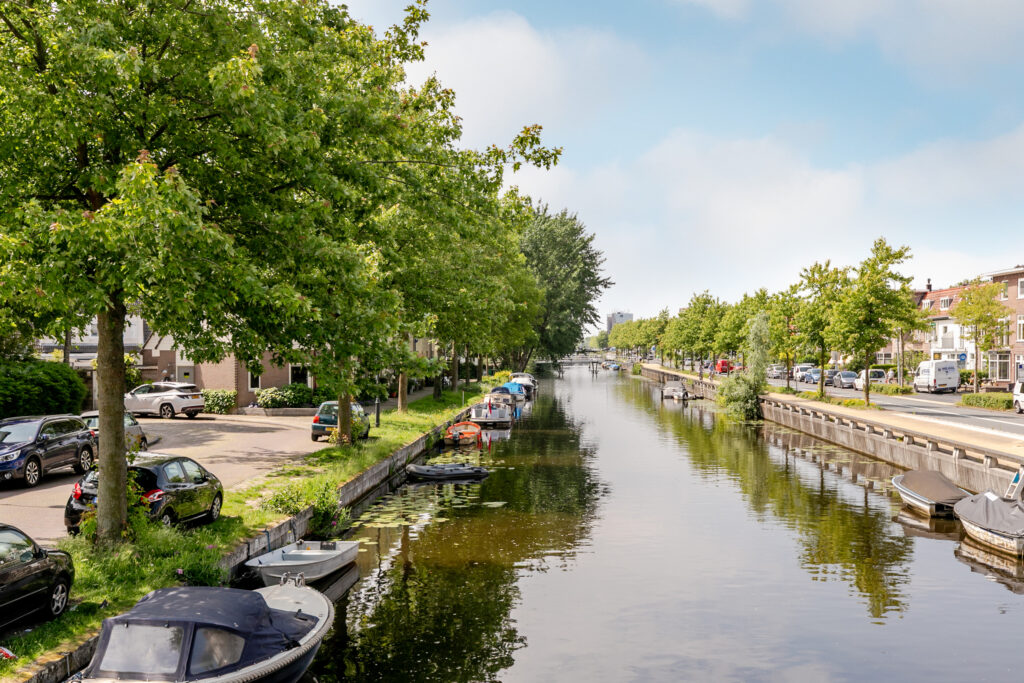Tree-lined canal with parked boats and cars.