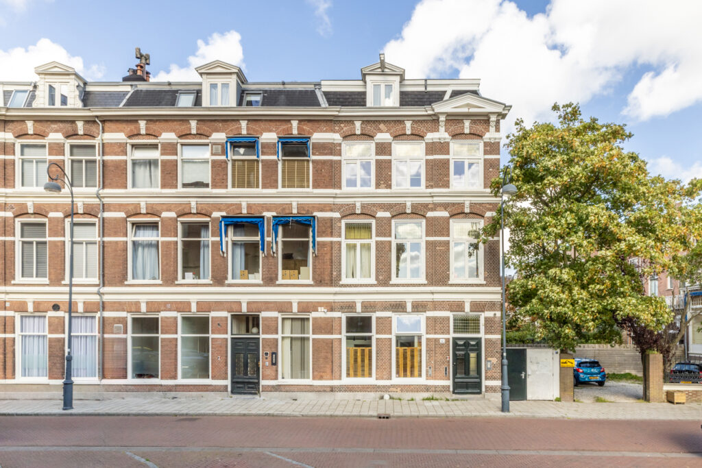 Brick apartment building with blue awnings, street view.