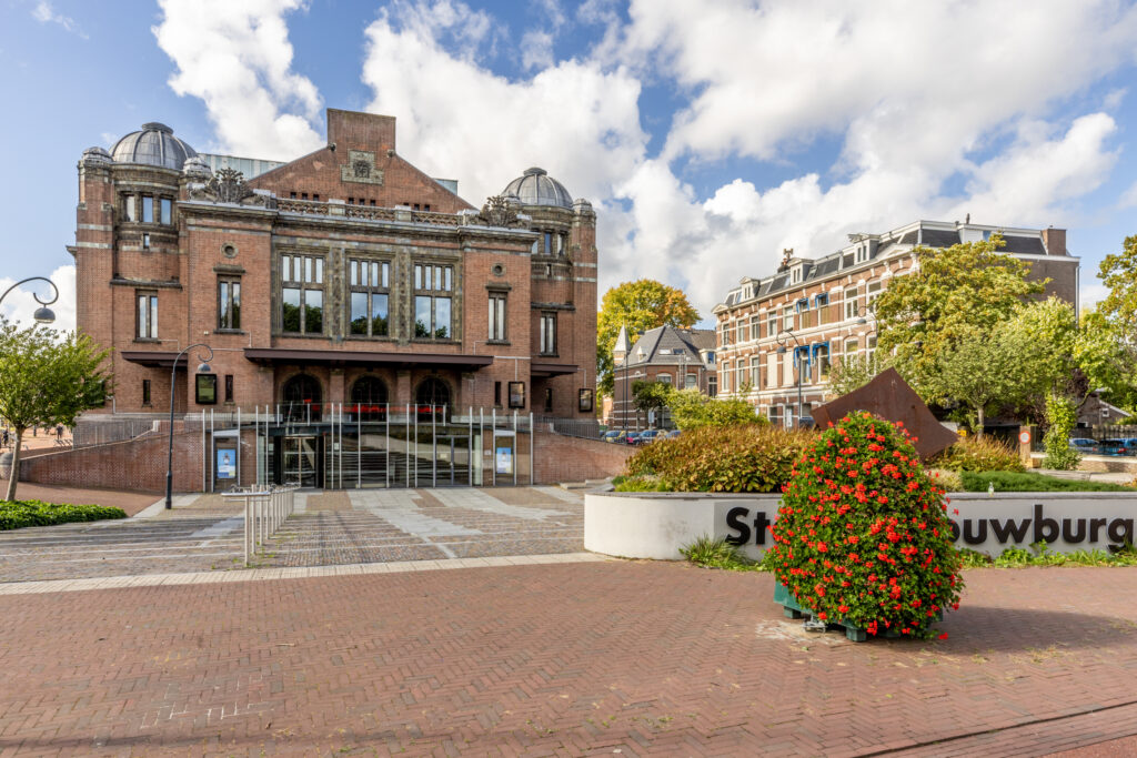 Historic theater building with red flowers outside.