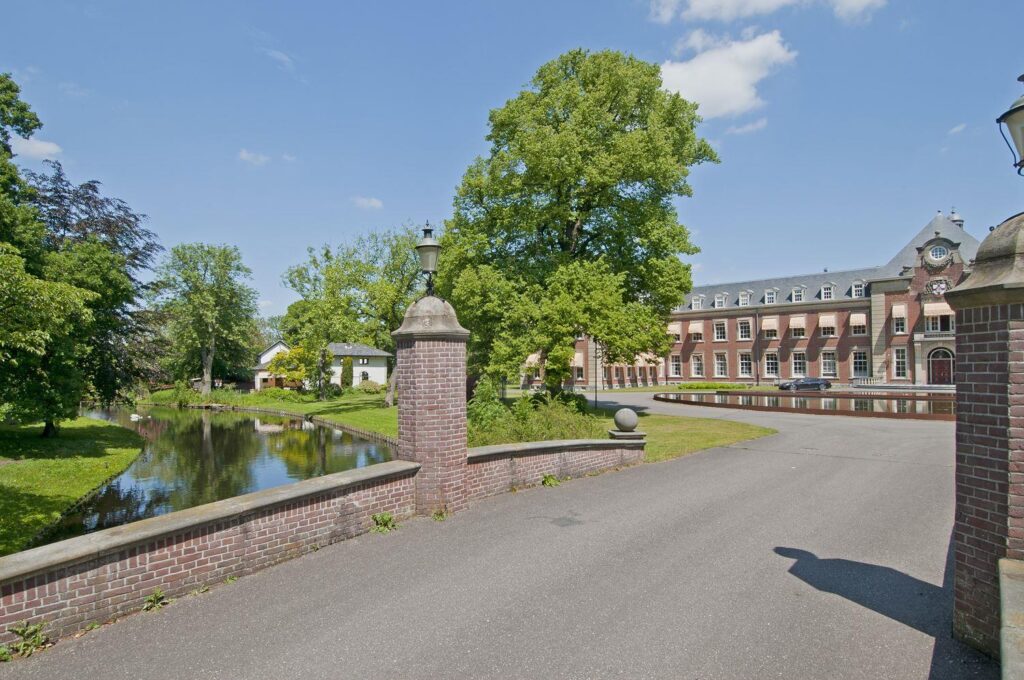 Historic manor with trees and pond in foreground.