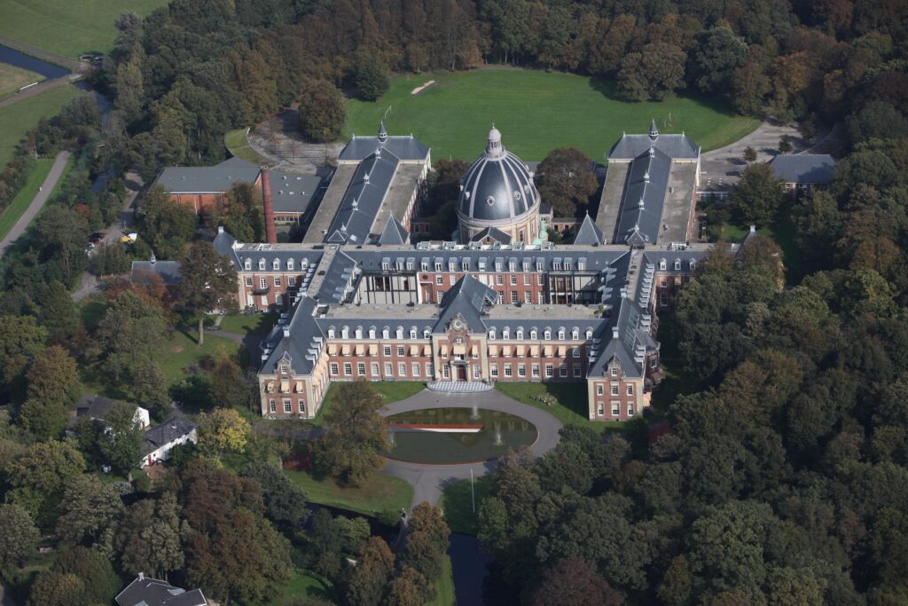 Aerial view of historic large building surrounded by greenery.