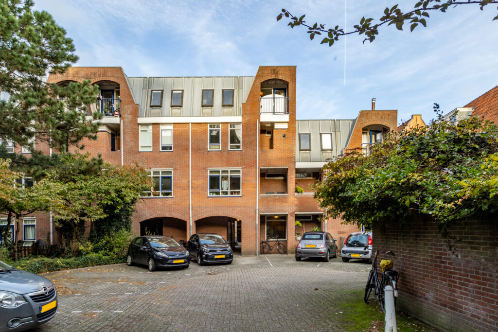 Brick apartment building with parked cars and bicycles.