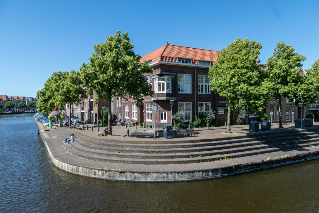 Canal with brick buildings and trees along sidewalk.