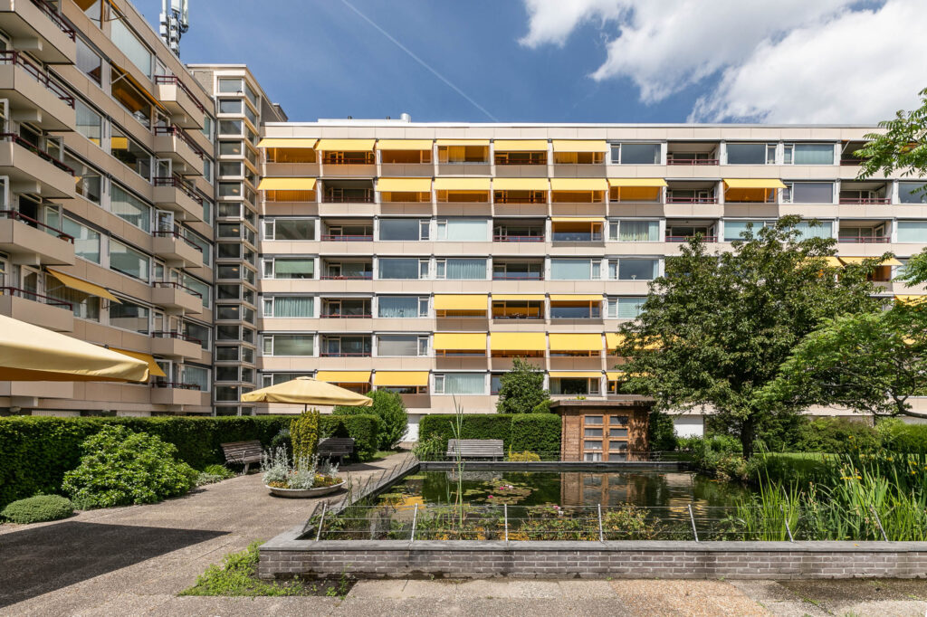 Modern apartment building with gardens and pond.