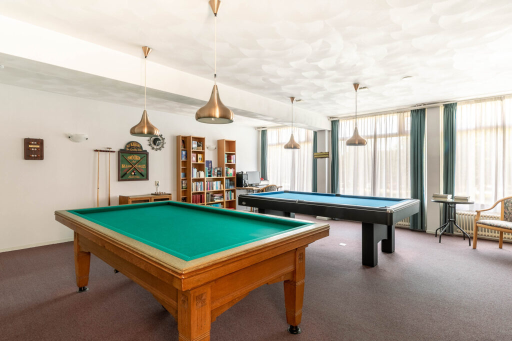 Room with billiard and pool tables, modern lighting.