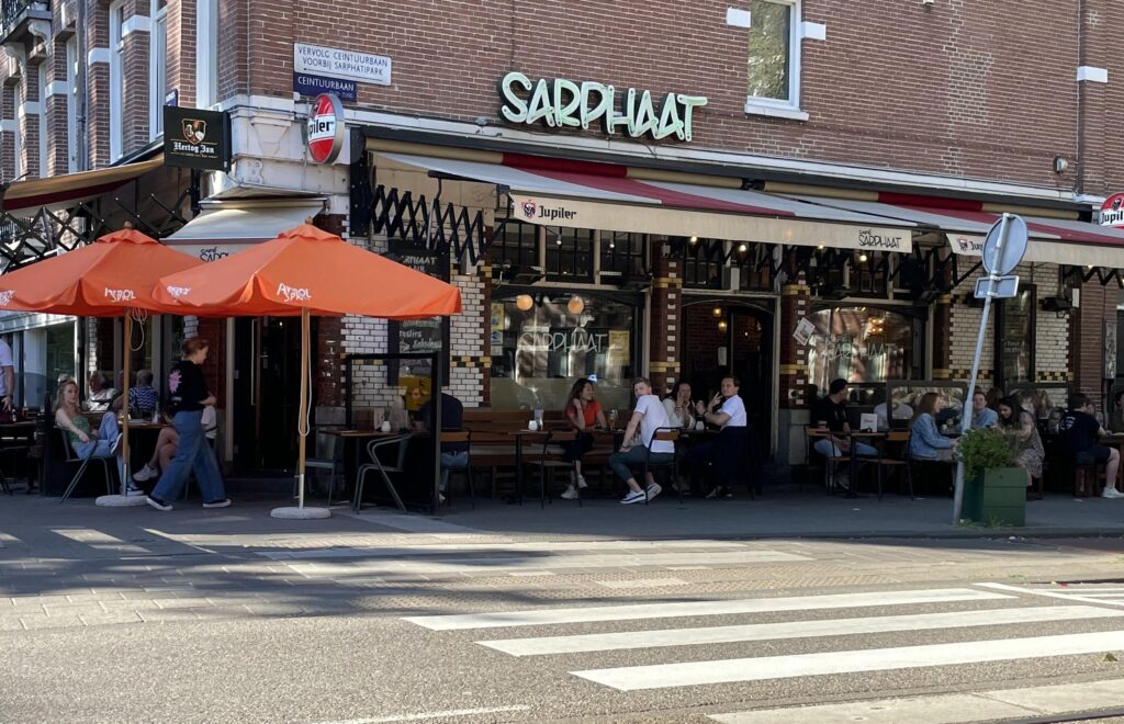 Outdoor cafe seating with orange umbrellas on street corner.