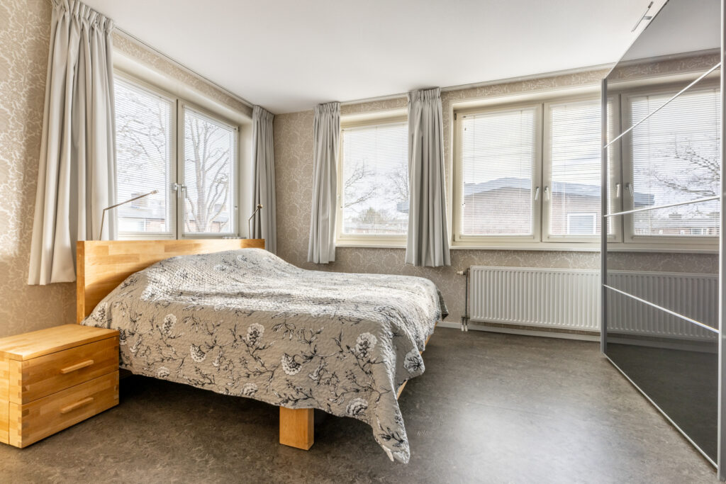 Cozy bedroom with wooden bed and large windows.