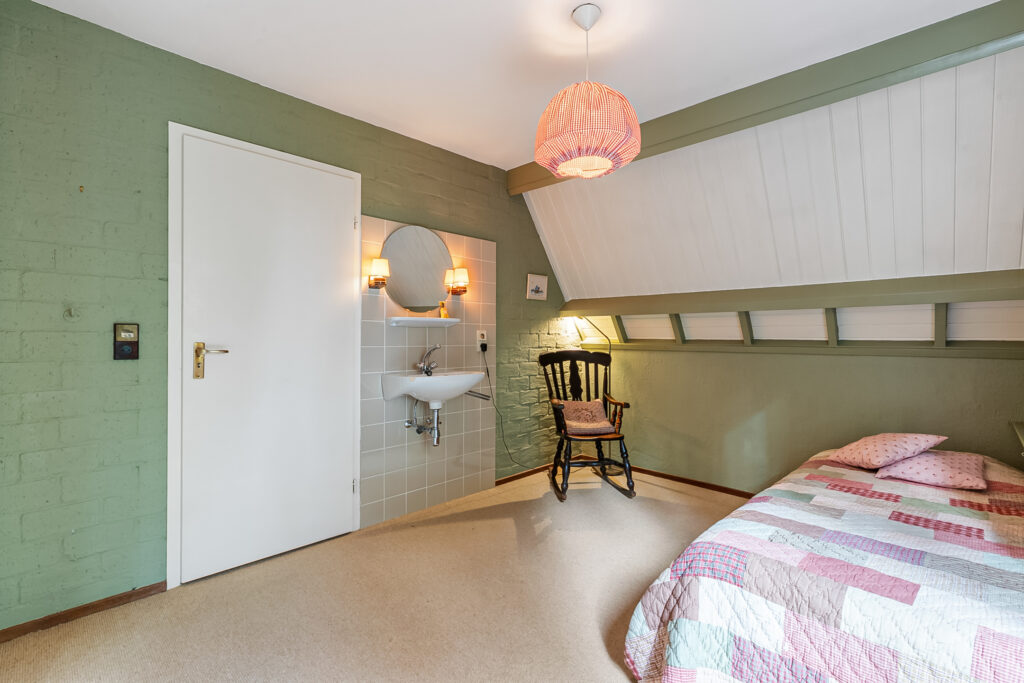 Cozy bedroom with sink, chair, and colorful quilted bed.
