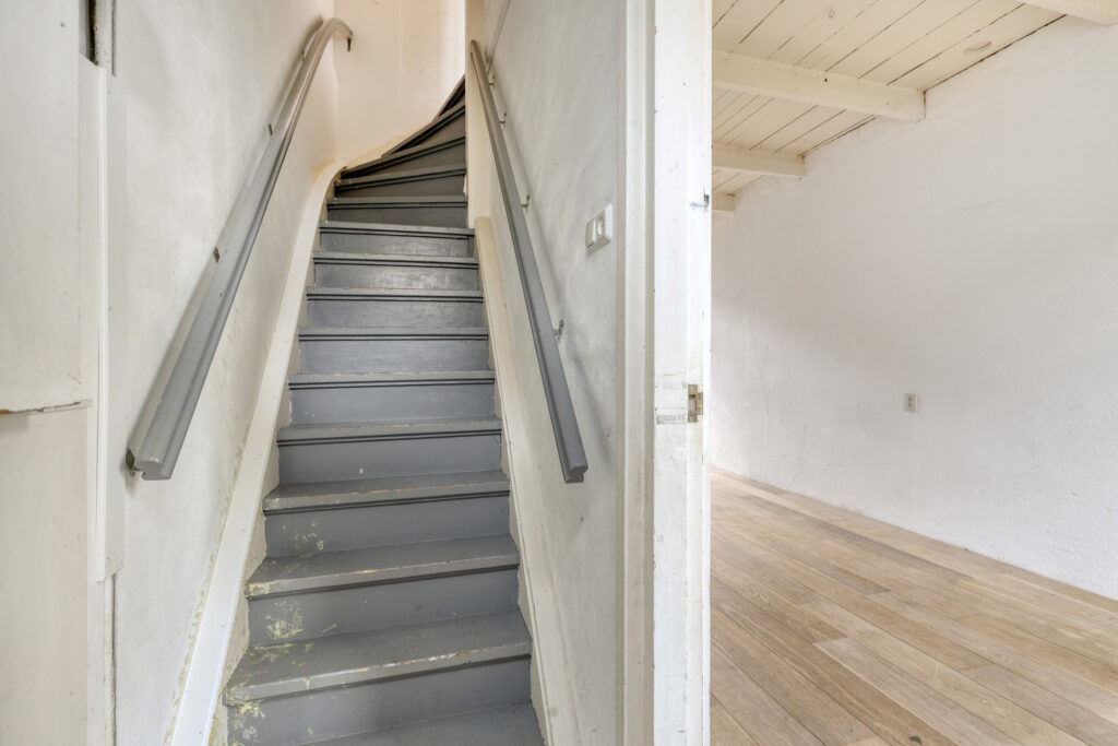Narrow wooden staircase with handrail in a hallway.