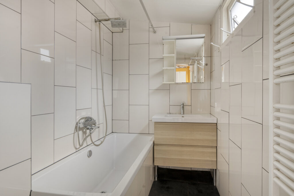 Modern white tiled bathroom with bathtub and sink.