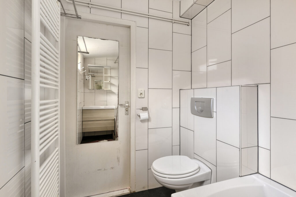 Modern white-tiled bathroom with toilet and mirror.