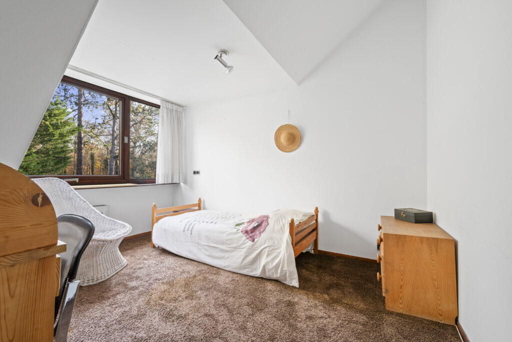 Cozy bedroom with window, bed, and wicker chair.