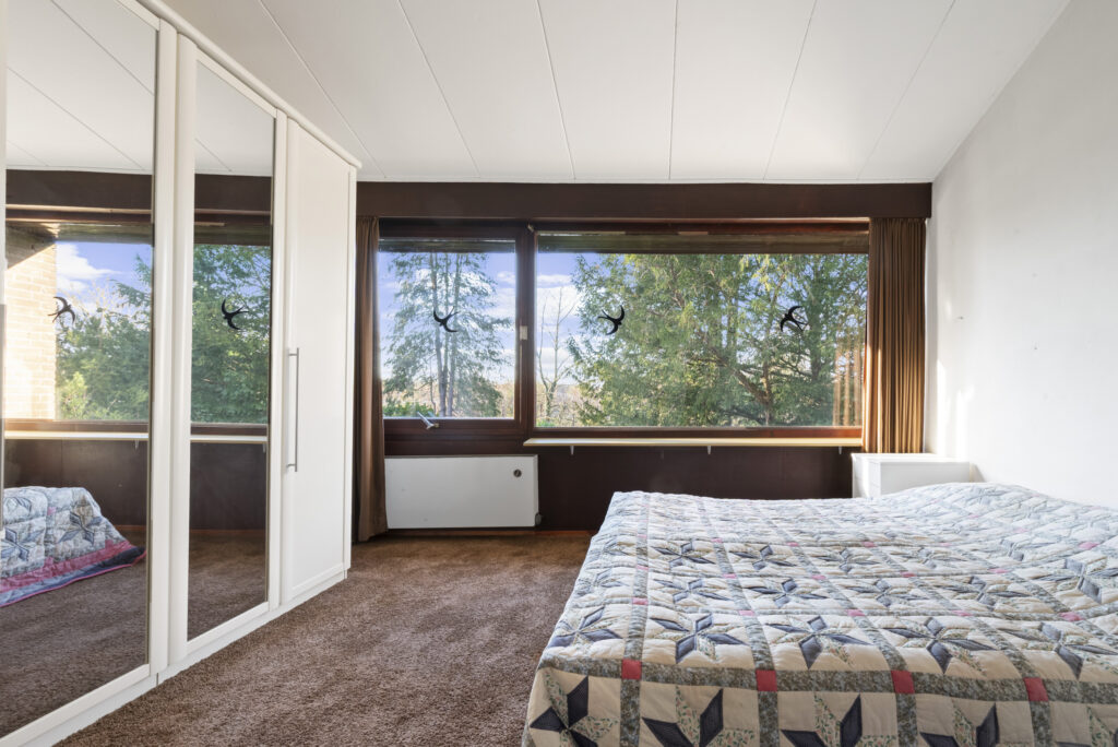 Cozy bedroom with large windows and mirrored closet.