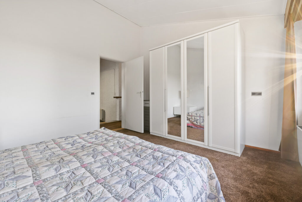 Bright bedroom with mirrored wardrobe and door ajar.