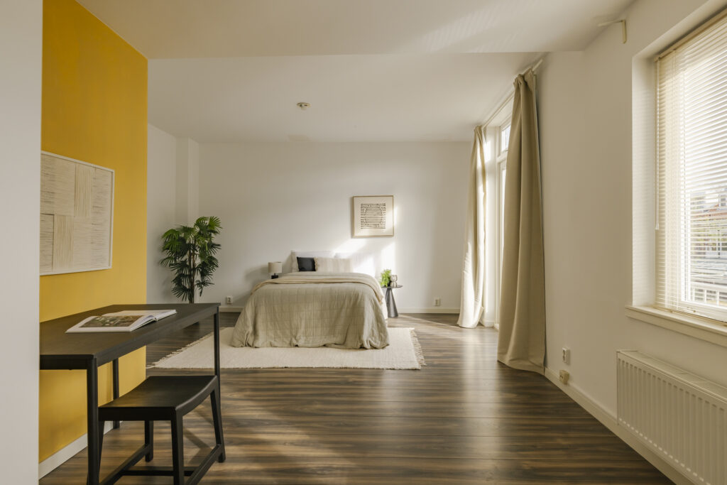 Modern bedroom with wooden floors and yellow accent wall.