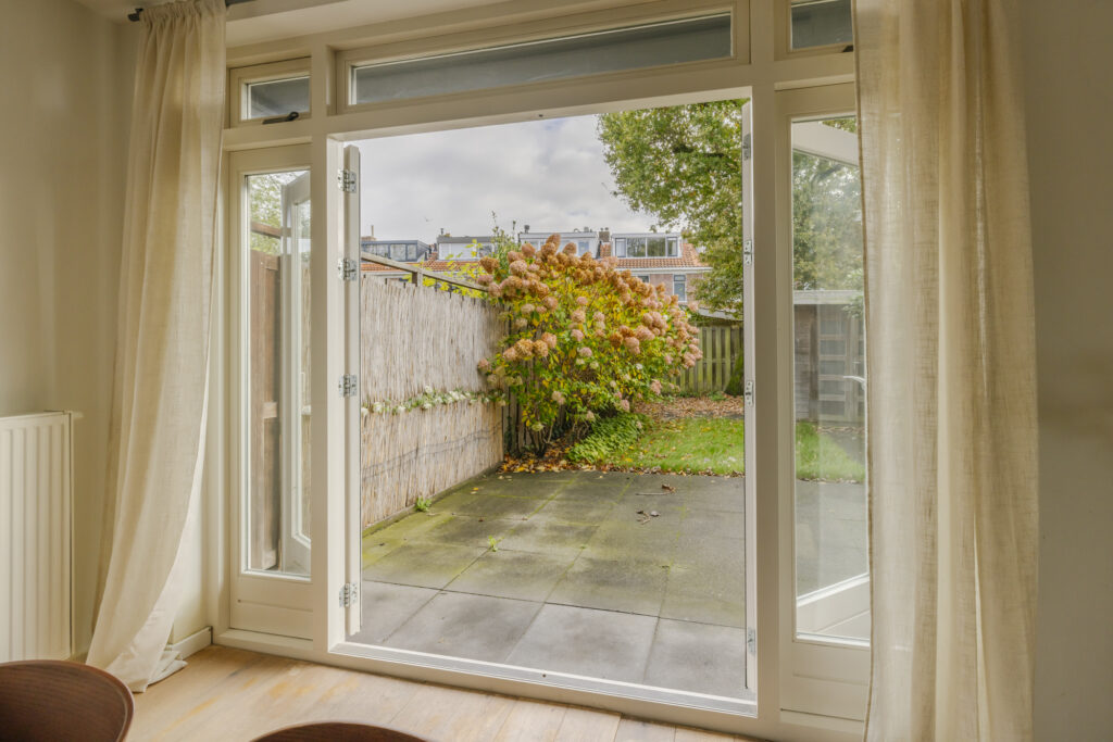 Open patio door to garden with shrubbery.