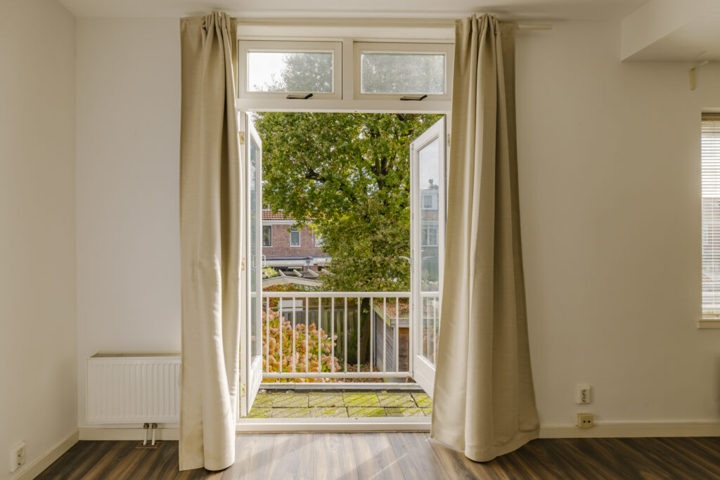 Open balcony door with view of garden trees.