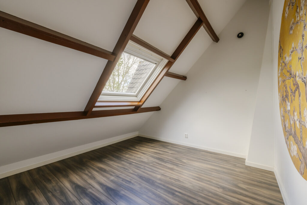 Empty attic room with skylight and wooden beams.