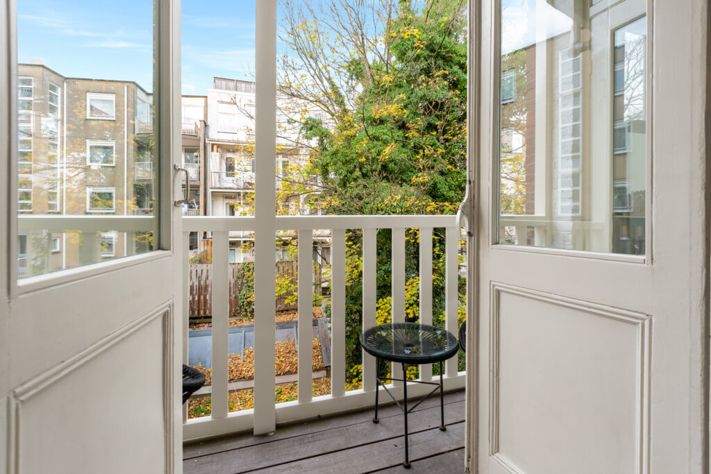 Open balcony doors, view of trees and buildings.
