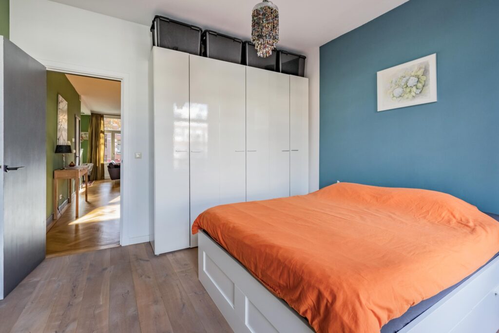 Modern bedroom with orange bedding and white wardrobe.